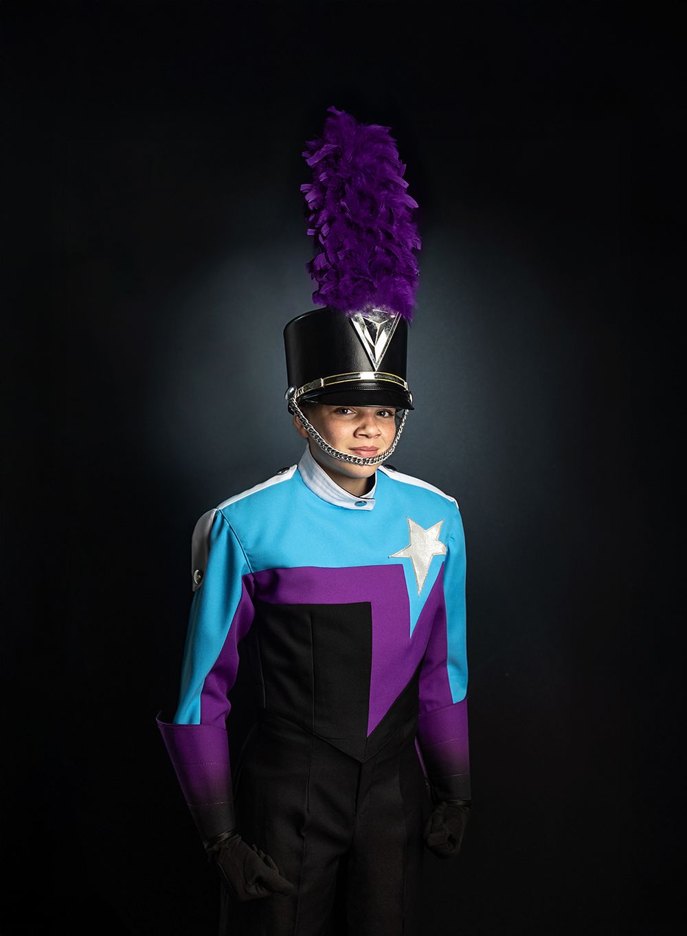 Performer in black top hat and suit with bright blue and purple accents poses dramatically against dark background.