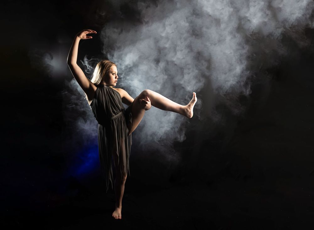 Silhouetted dancer performs graceful movements against dark background with atmospheric smoke effects.
