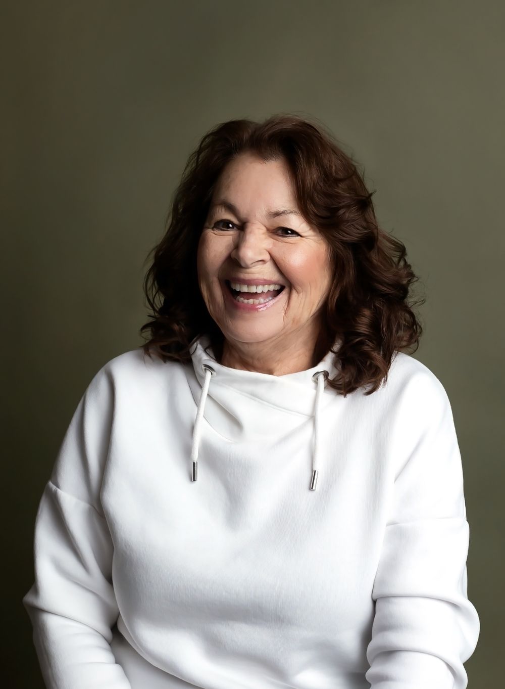 A person in a white hoodie sweatshirt smiles warmly against a dark green background in a series of expressive poses.
