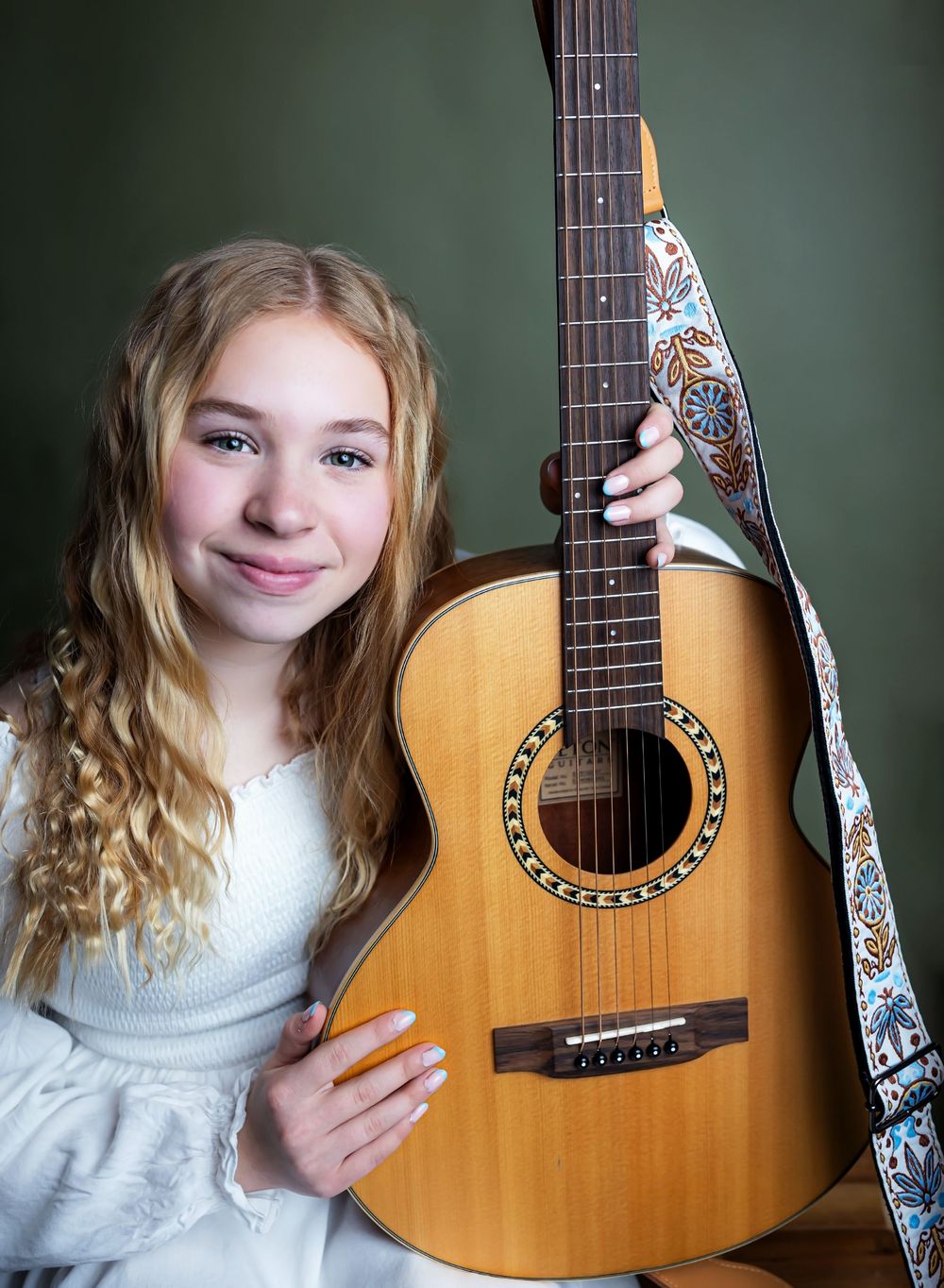 A series of four photos showing an acoustic guitar with decorative strap against a dark green background.
