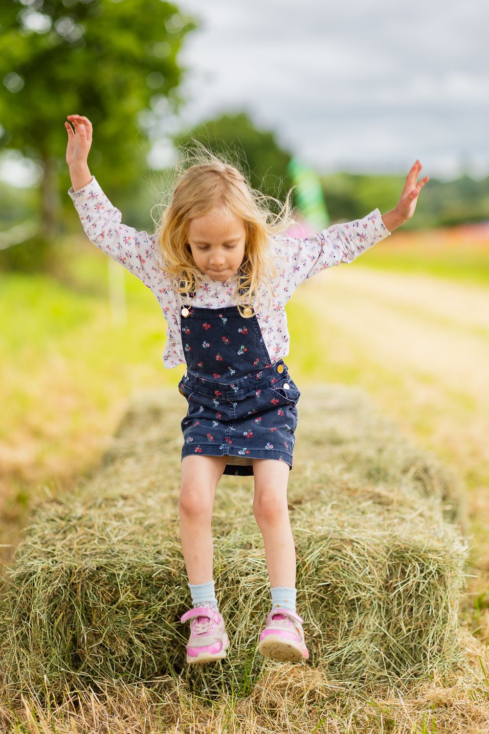 Photo of a young girl jumping from a bail of hay.