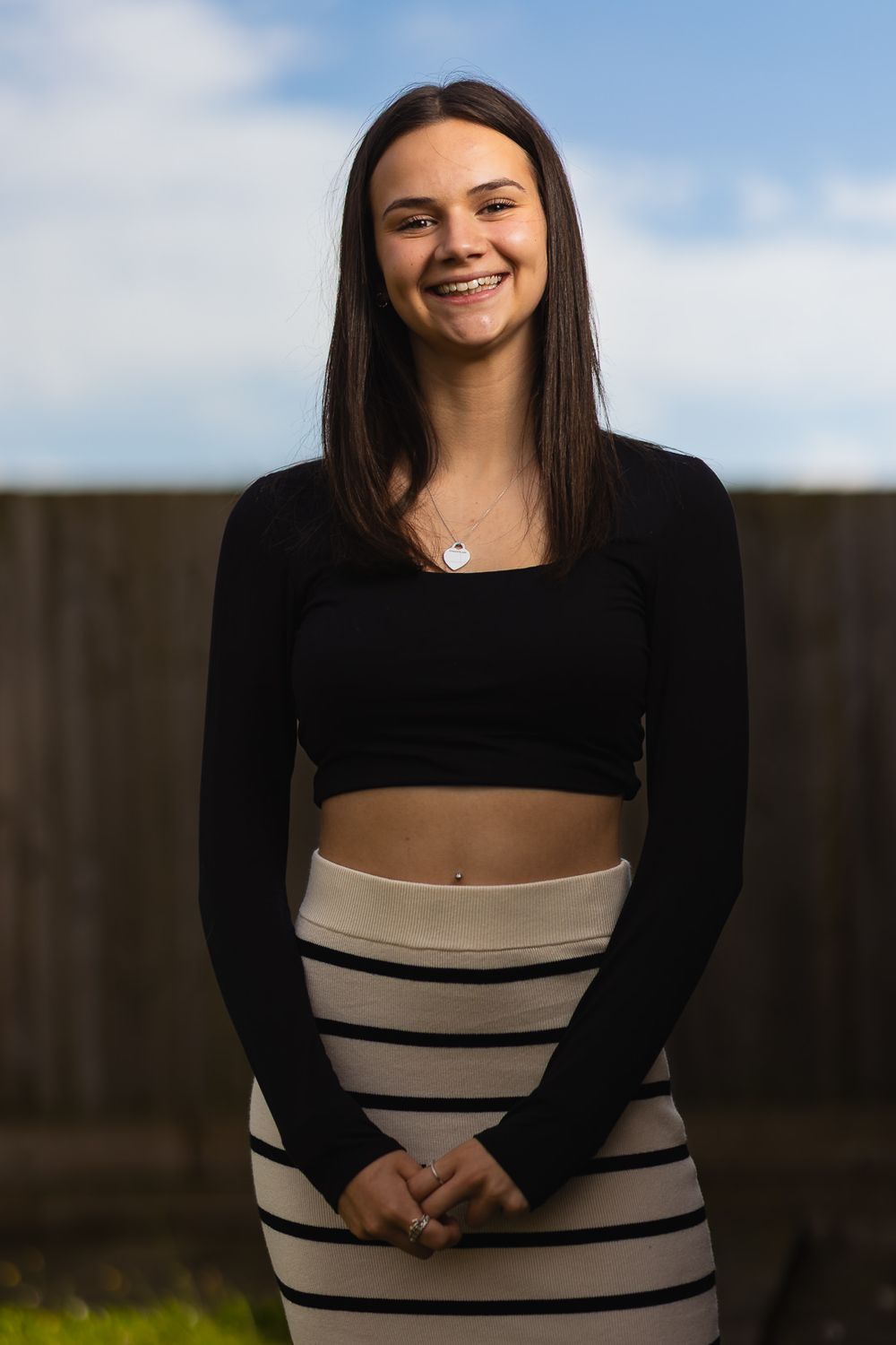 Portrait photo of a teenage girl, smiling and wearing smart casual summer attire. Outdoors with a blue sky background