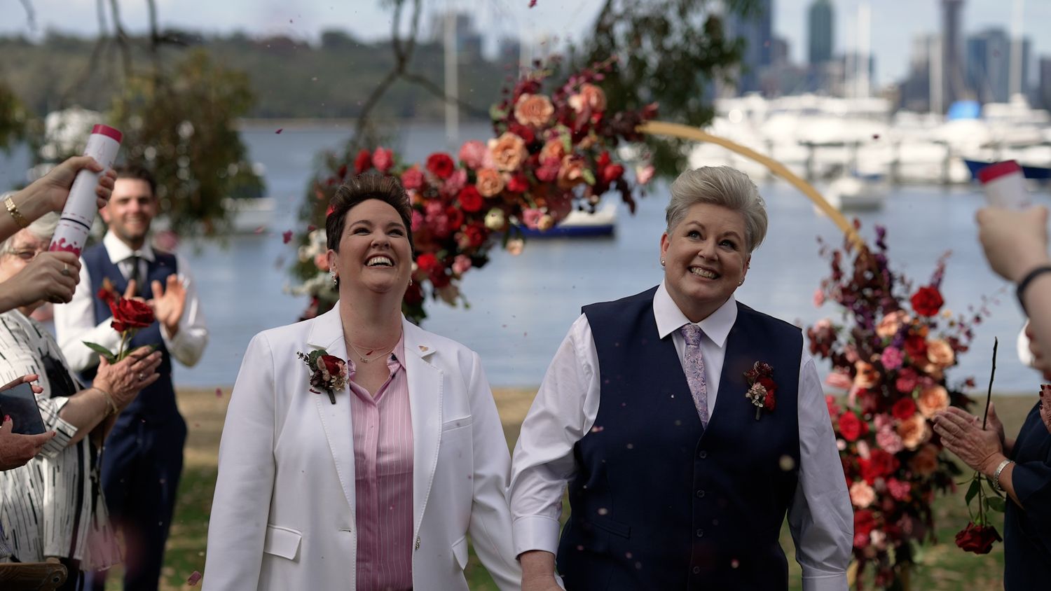 Wedding party celebrating outdoors with city skyline visible in background.