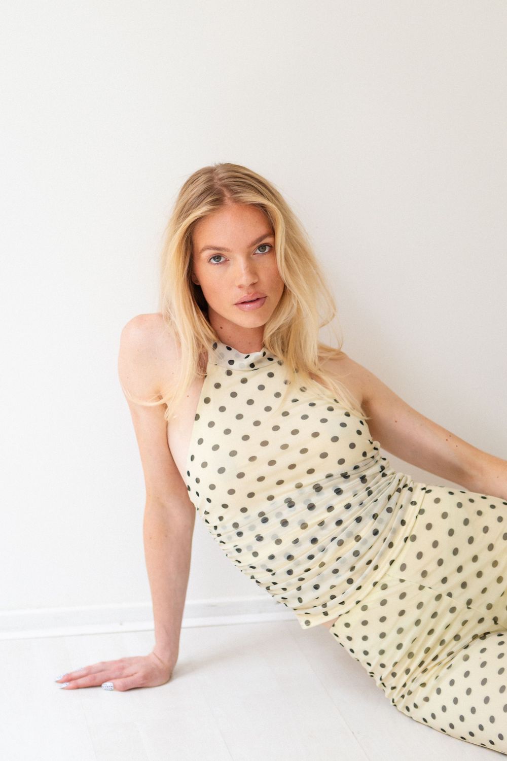 Model poses in cream colored polka dot dress against white background.
