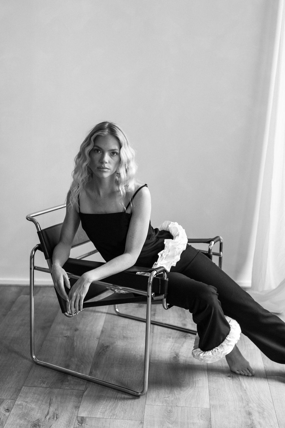 A stylish figure in black lounges gracefully across a modern silver metallic chair in an artistic photo series.