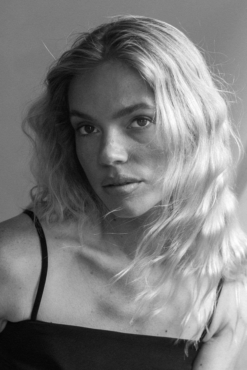 Black and white portrait of a person with wavy blonde hair and intense gaze looking directly at camera.