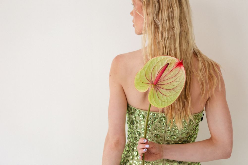 A light green anthurium flower is held against a white studio backdrop.