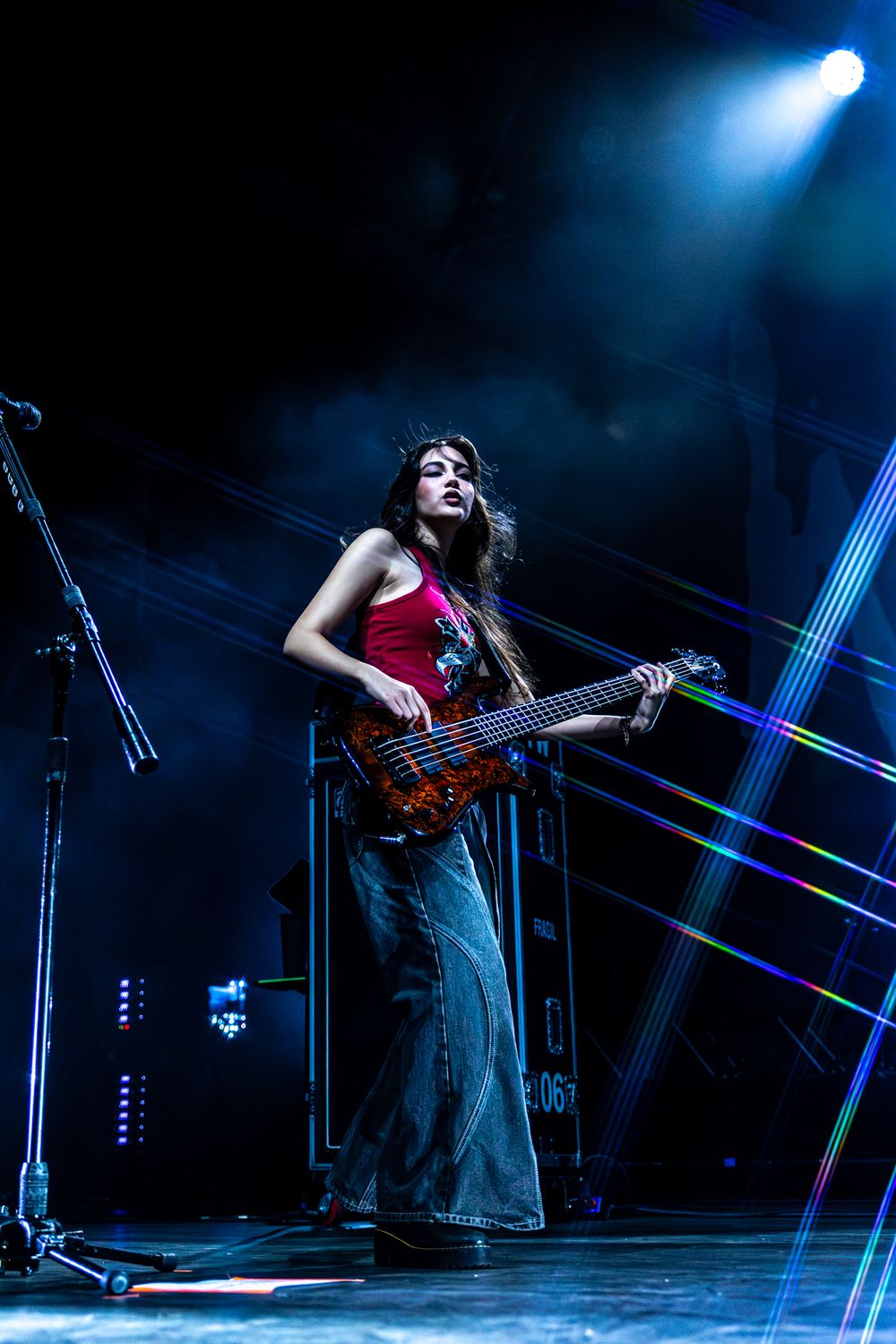 Musician plays guitar on dimly lit stage with striking blue spotlights and dramatic shadows.