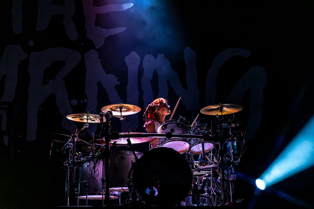 Concert stage setup with drum kit illuminated by dramatic blue spotlights.