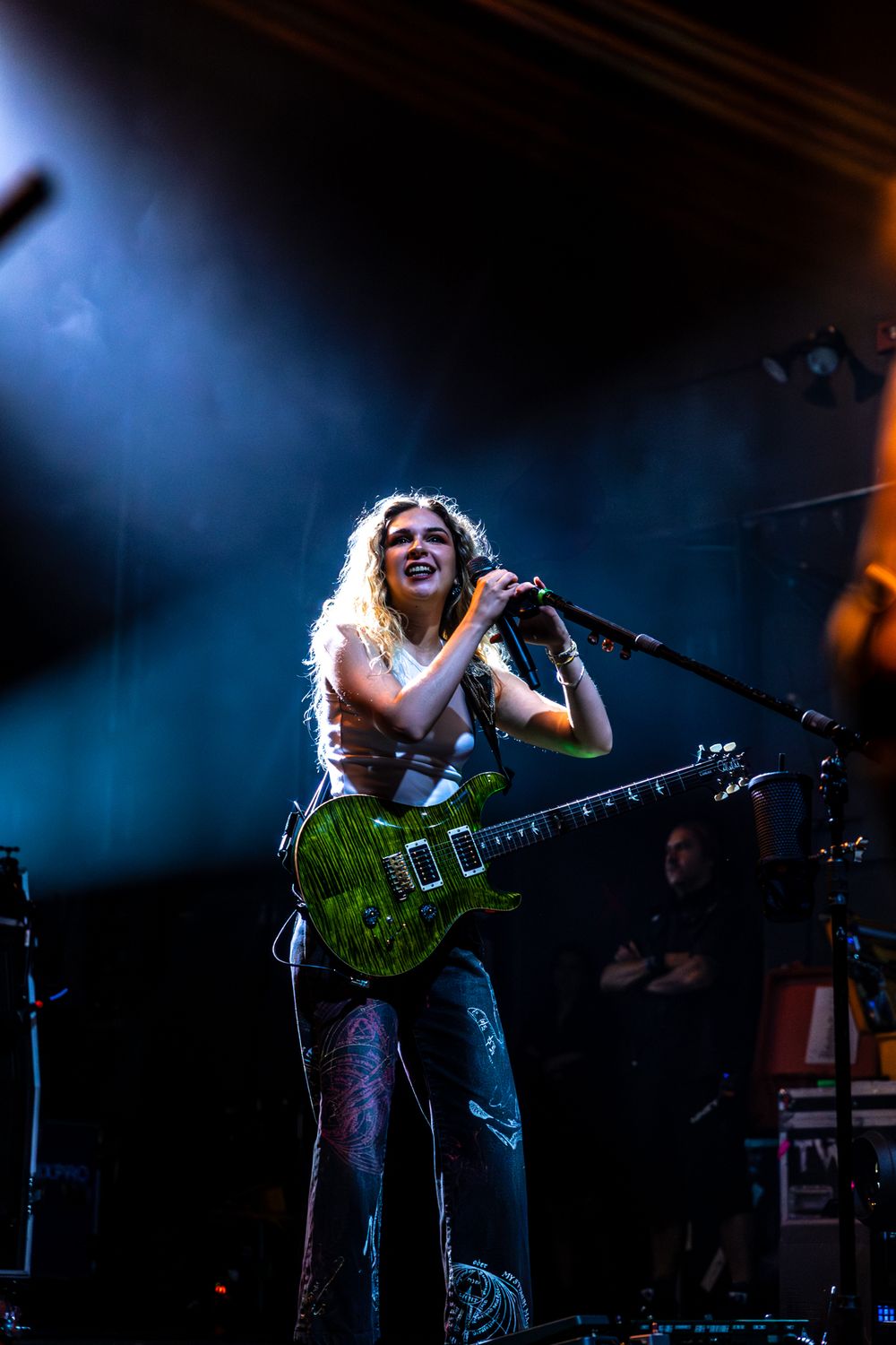 A musician performs passionately on stage with a guitar under dramatic blue stage lighting.