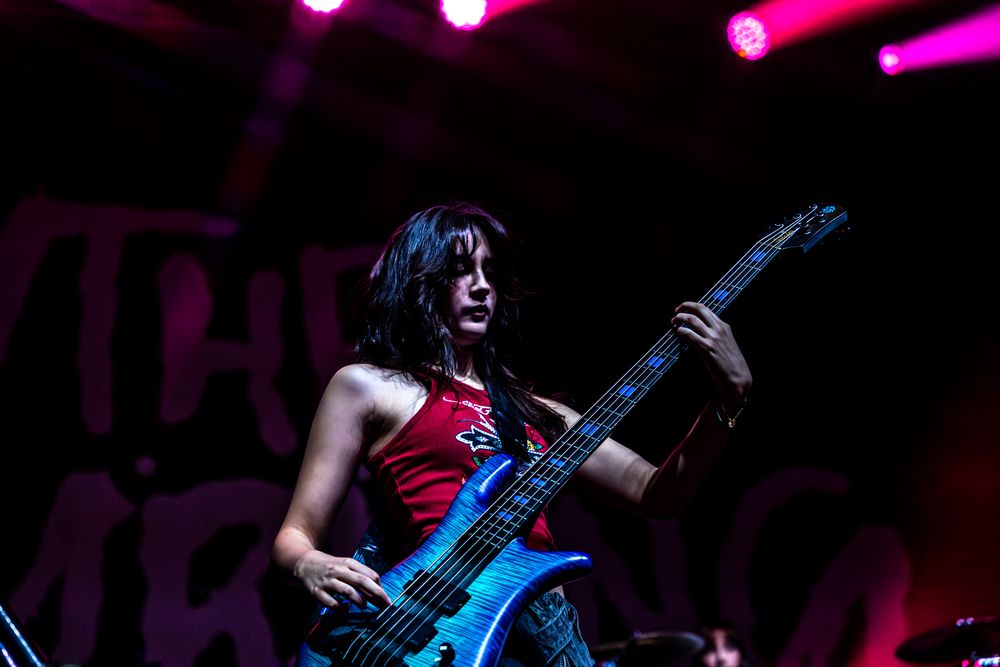 Guitarist plays energetically on darkened stage with pink and purple lighting effects.