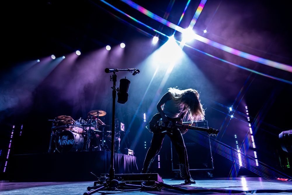 Wide angle concert stage view with dramatic blue and purple lighting creating silhouettes of musical equipment.