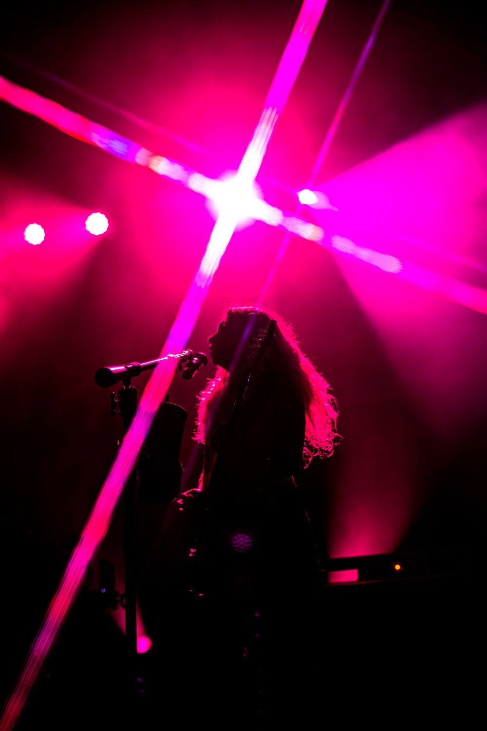 Abstract concert lighting in vivid pink and purple hues creating dramatic silhouettes on a dark stage.