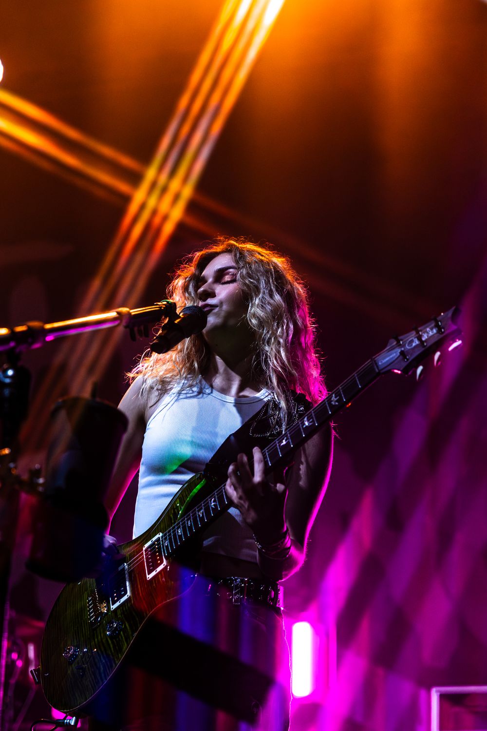 Rock performer silhouetted against vibrant orange and purple stage lighting during an energetic show.
