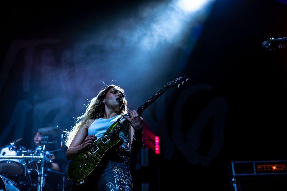 A dramatic concert performance with blue stage lighting illuminating musicians on stage during a live show.