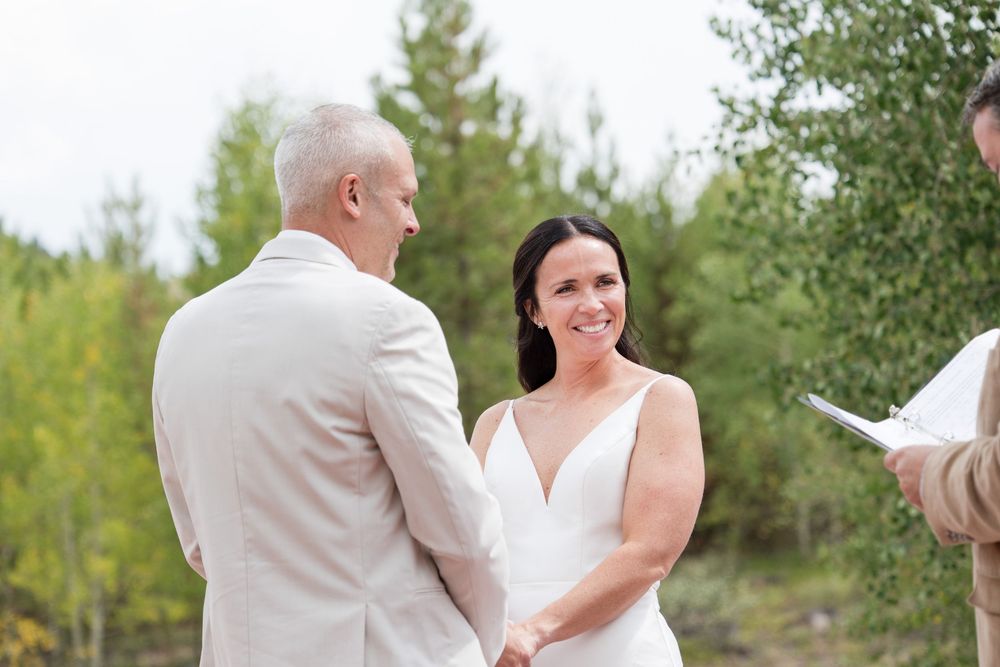 A couple in wedding attire shares an intimate moment while reading vows during an outdoor ceremony in a garden setting.