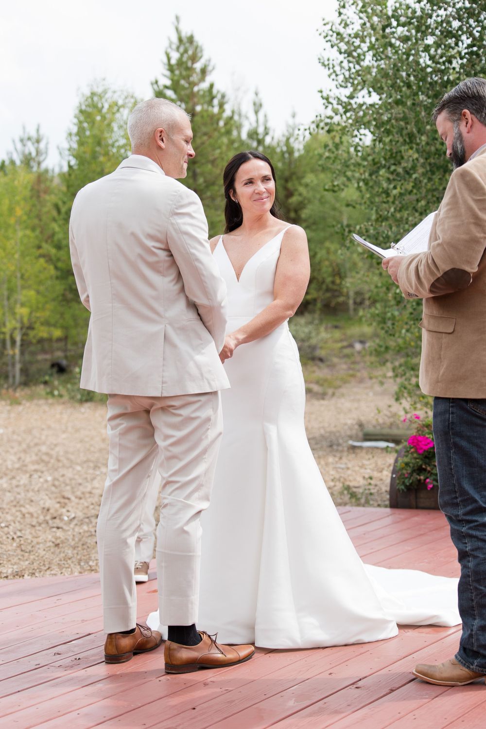 Wedding ceremony detail showing formal attire and wooden deck with forest backdrop in natural outdoor setting.