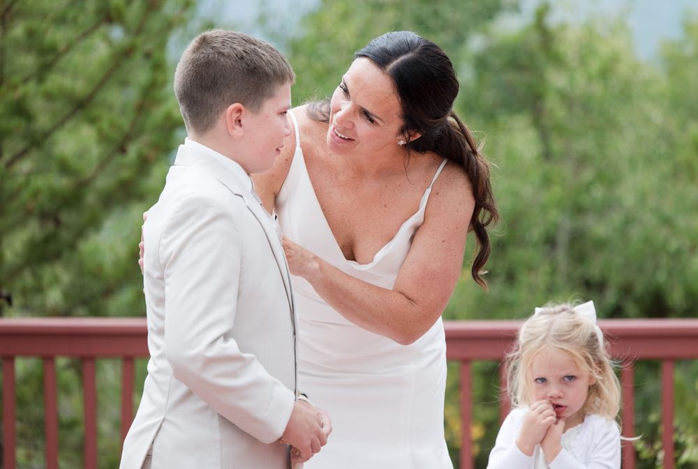 A tender moment shared between a couple in white during their wedding ceremony with a young child looking on.