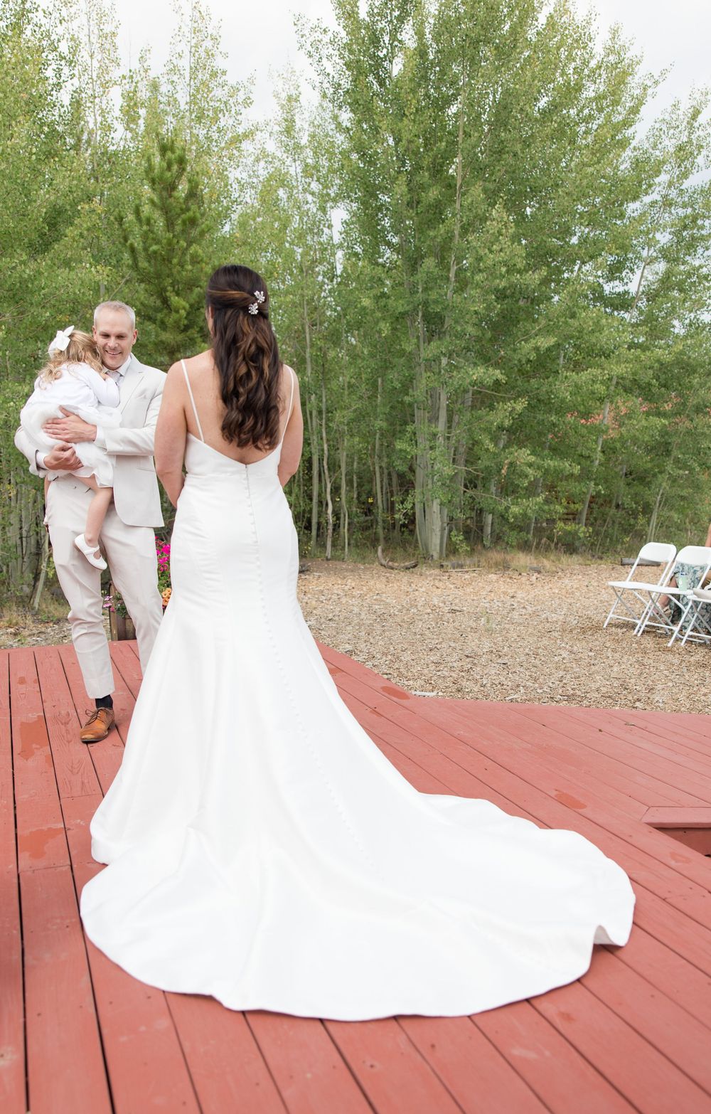 A wedding ceremony on a red wooden deck with a beautiful white bridal gown train and aspen trees in the background.