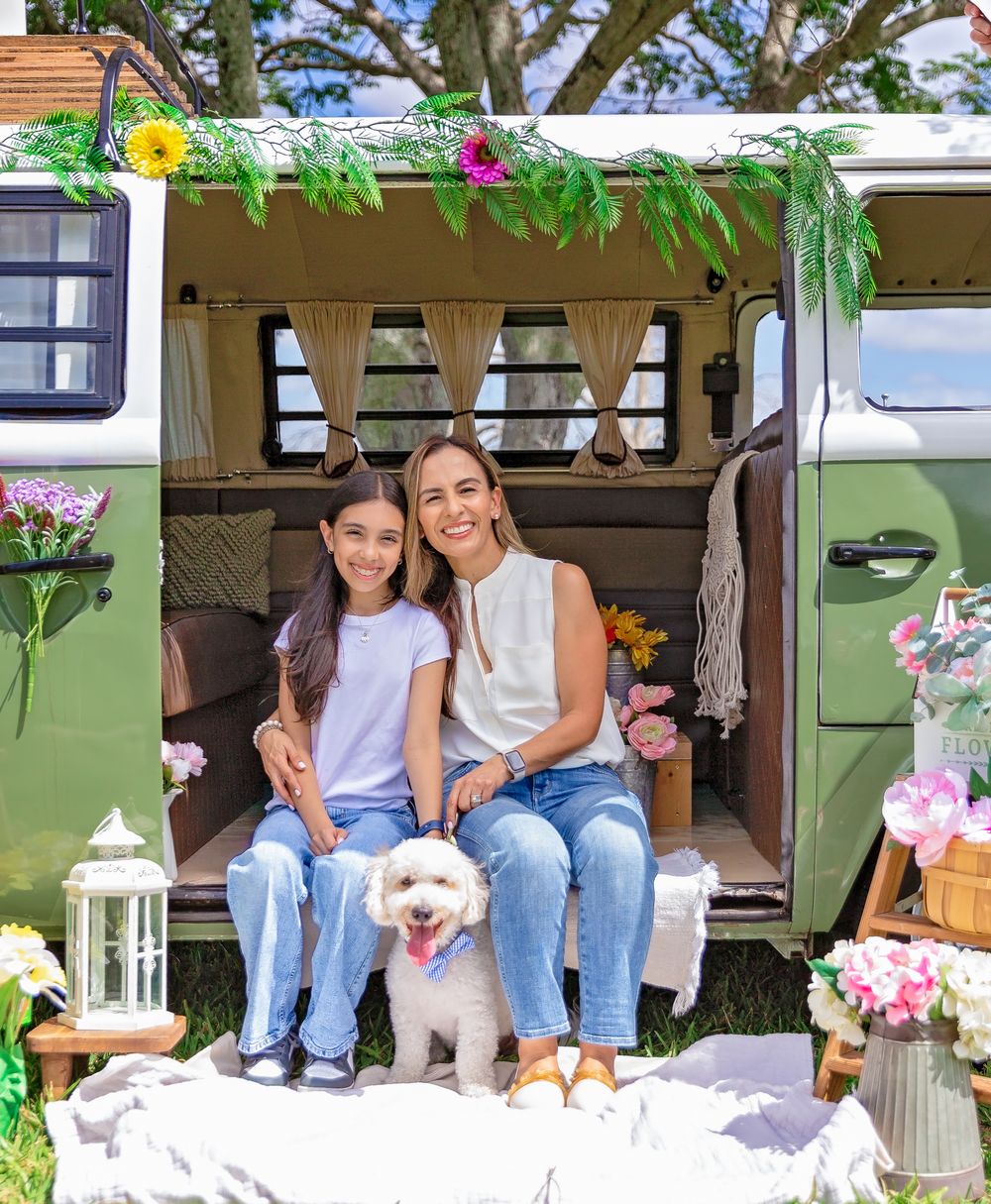 Small white dog sit with their owners in a decorated outdoor setting with flowers and lanterns.