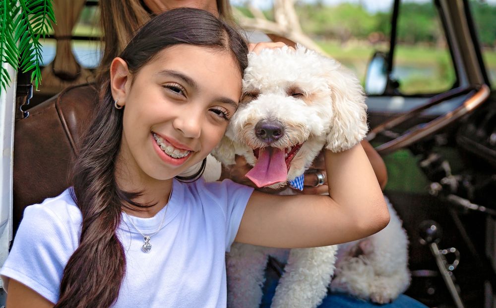 White fluffy dogs pose with their owners in a sunny outdoor setting.