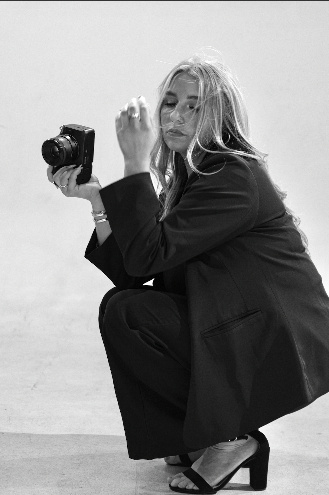 A black and white fashion photo series showing a figure in dark clothing crouching in dynamic poses against a light background.