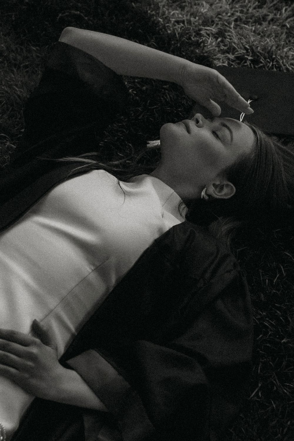 A series of black and white photos showing a person lying down in grass with dramatic shadows and lighting.