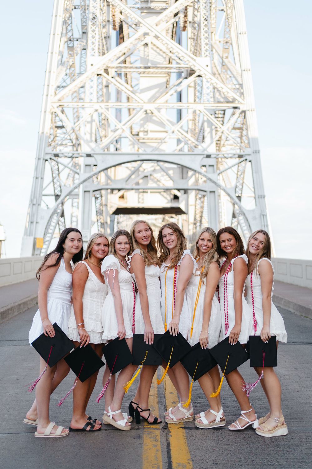Group of friends in matching white tops and black bottoms pose playfully on a bridge.
