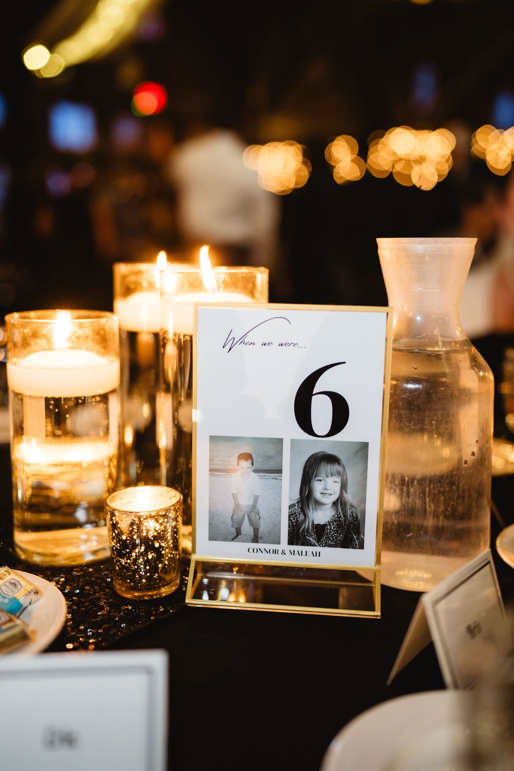 Wedding table number 6 card displayed with glowing candles and glass vase in romantic evening setting.