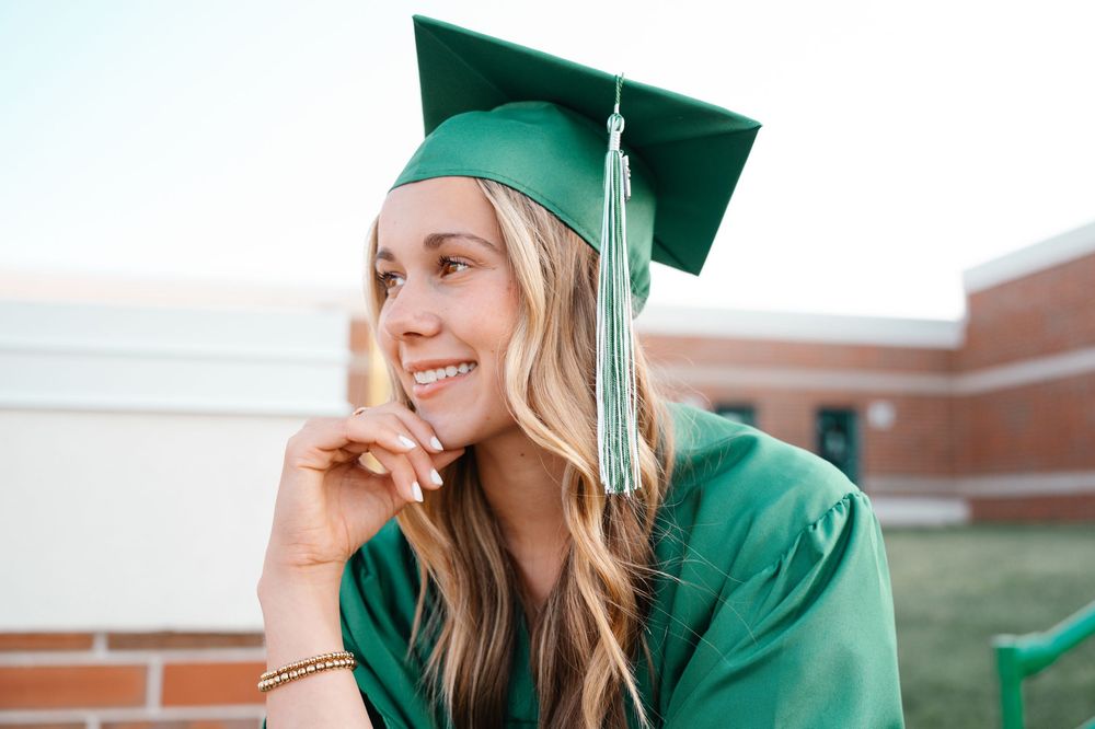 Smiling female graduate in green cap and gown posing outdoors at Waterford Union High School.