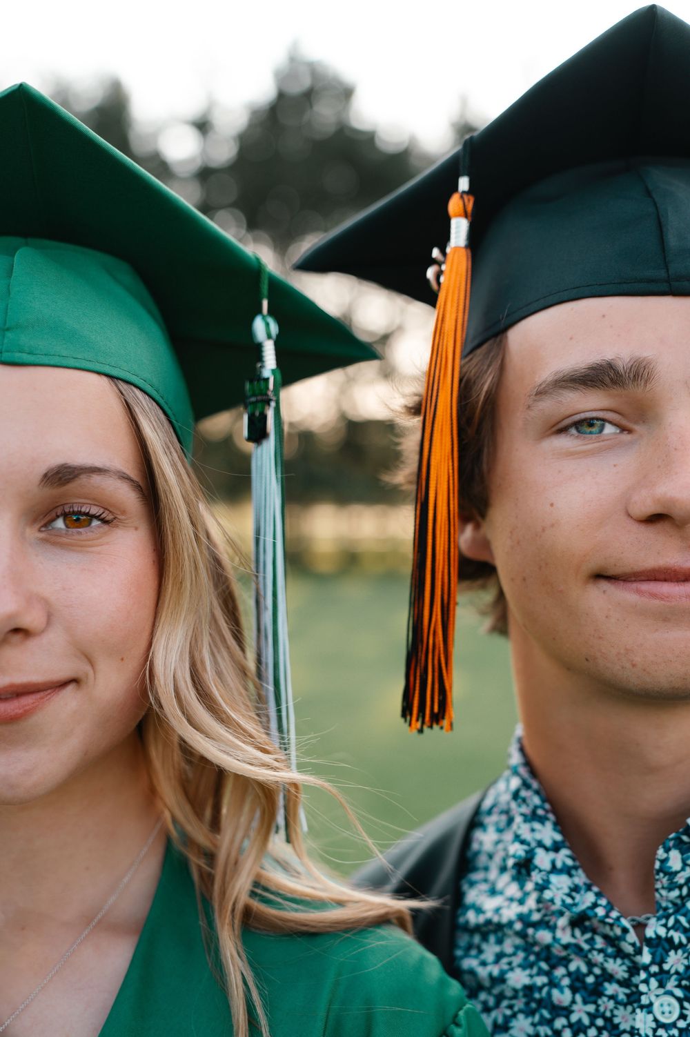 Close-up portrait of two graduates wearing green and black mortarboard caps with tassels.