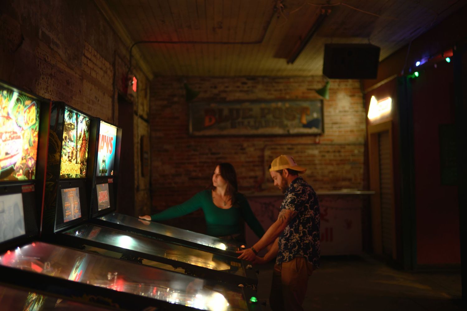 Dimly lit bar interior with arcade games and pool tables creating a retro gaming atmosphere.