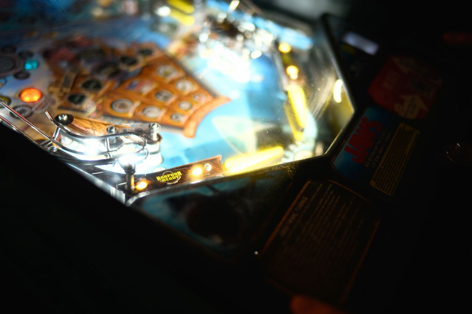 Close-up shot of an illuminated pinball machine playfield with colorful lights and reflections.