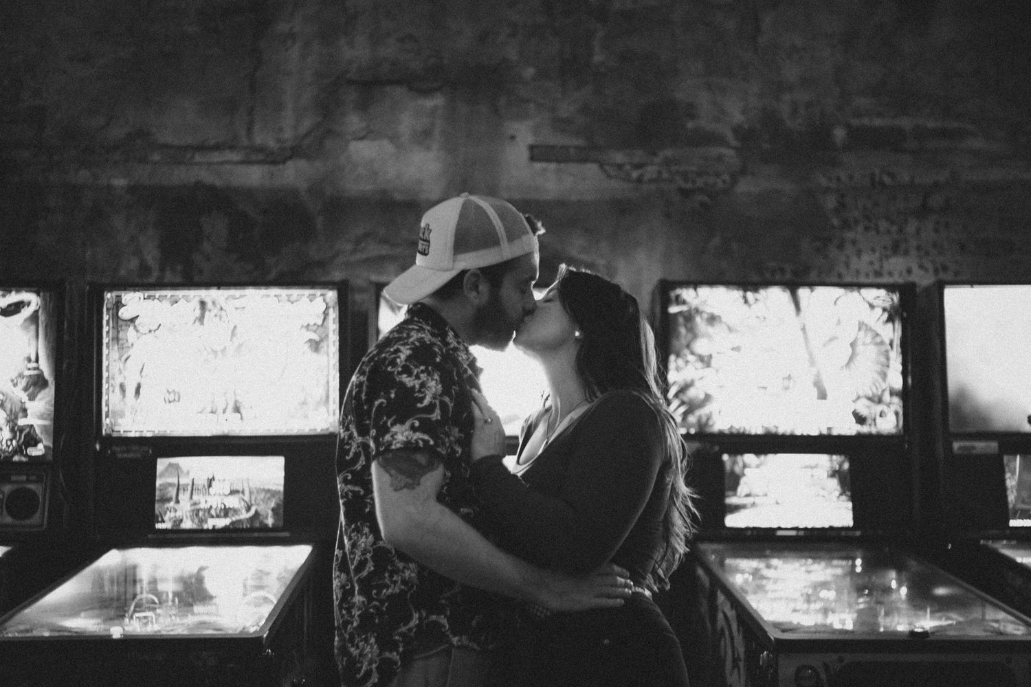 A romantic black and white moment shared between a couple in front of vintage arcade machines.