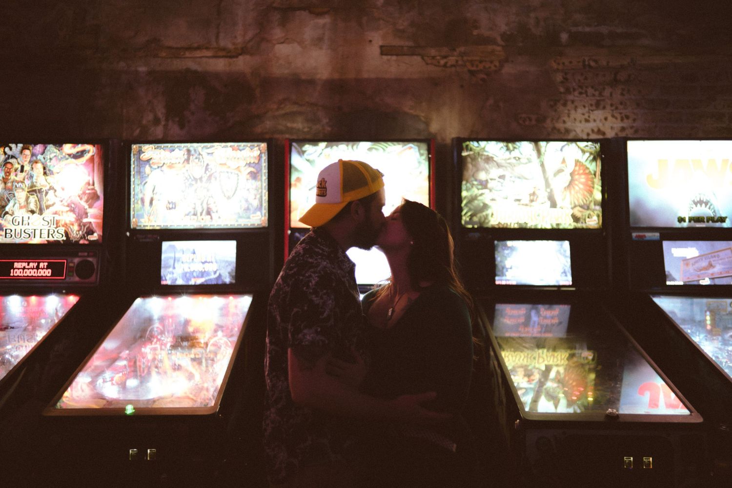 Row of illuminated arcade game cabinets line a dark wall in a gaming bar.