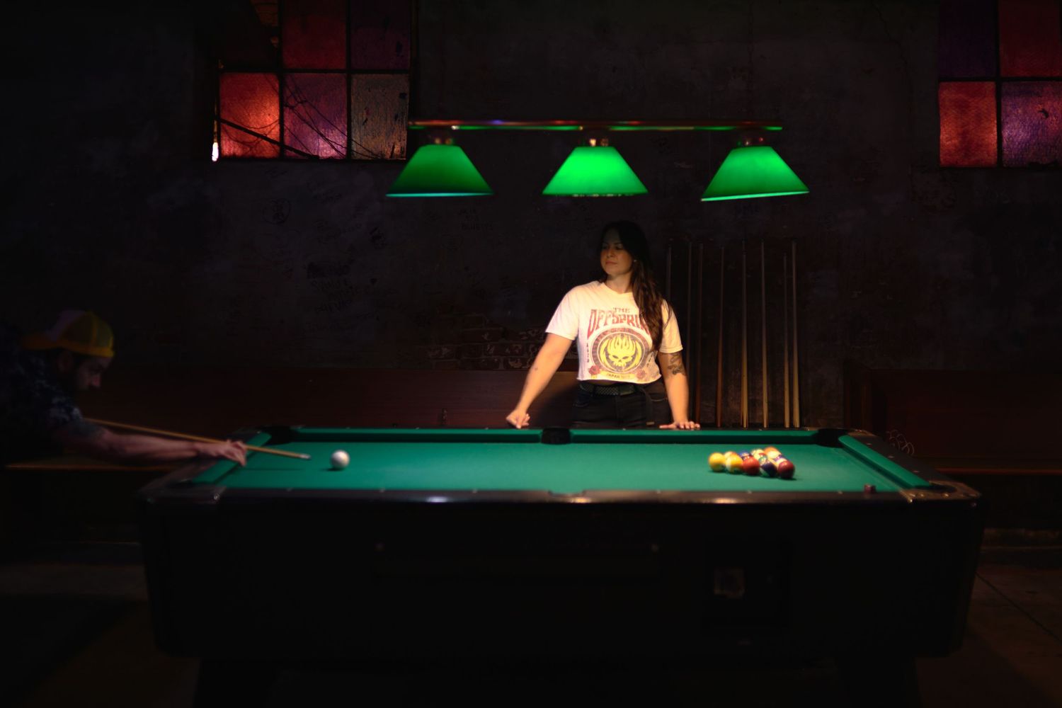 Green-lit pool table in a dark bar setting with ambient lighting.