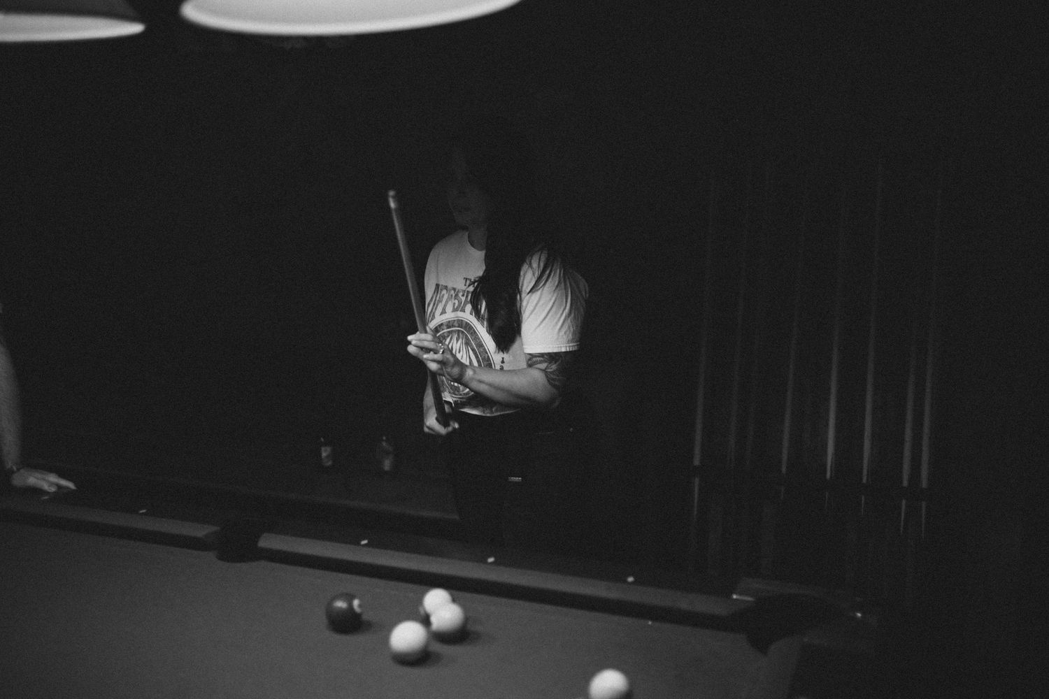 Black and white photo of a pool table in low-light bar setting.