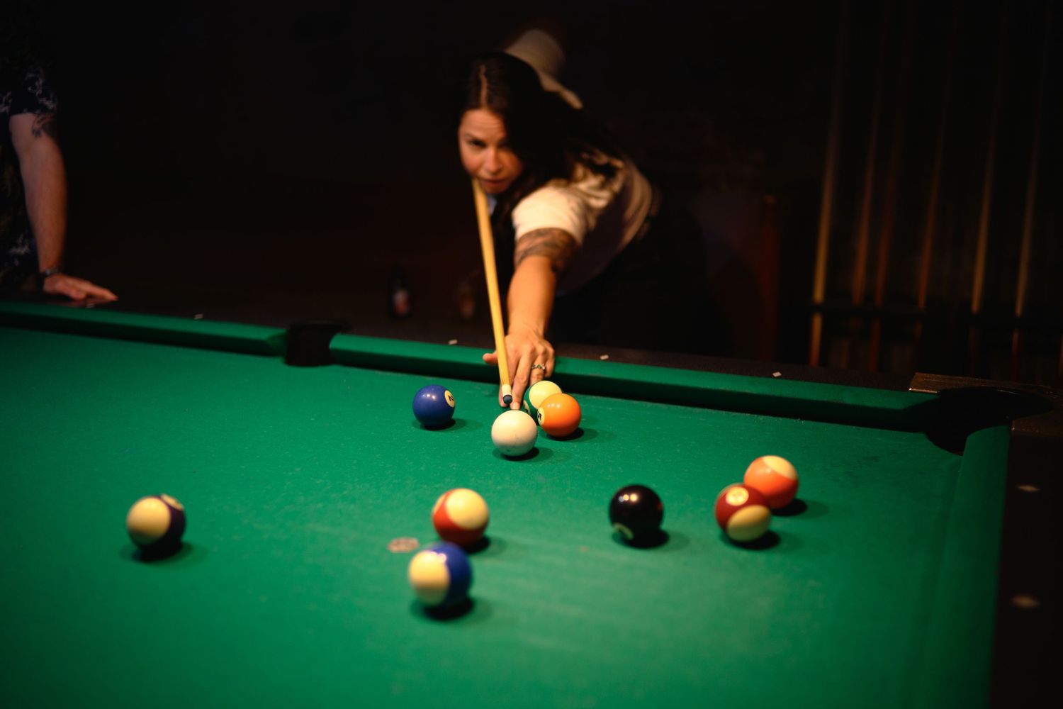 Player taking aim at pool balls on a green felt billiards table in dim lighting.