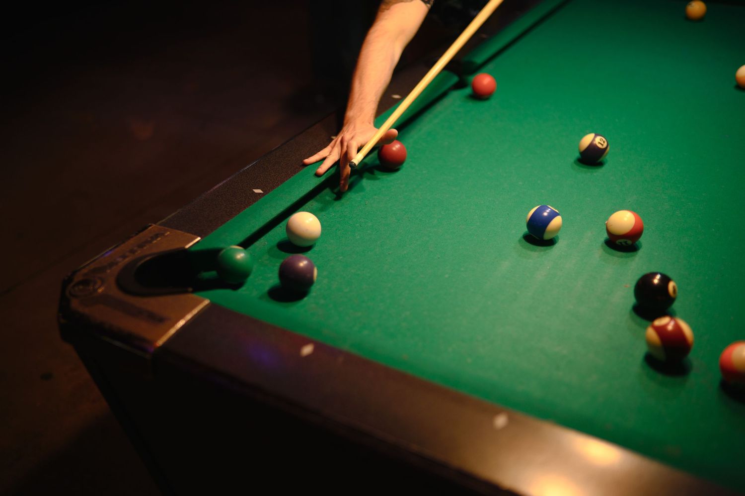 Close-up shot of a pool table with scattered billiard balls on green felt under dramatic lighting.