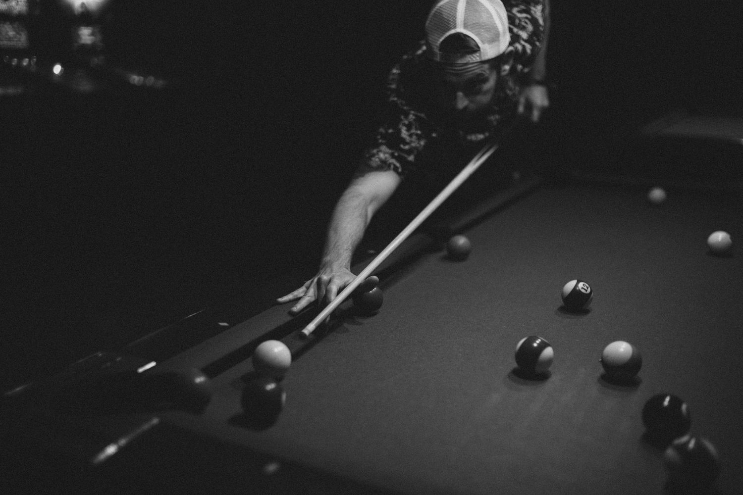 A black and white shot of a player lining up a shot on a pool table.