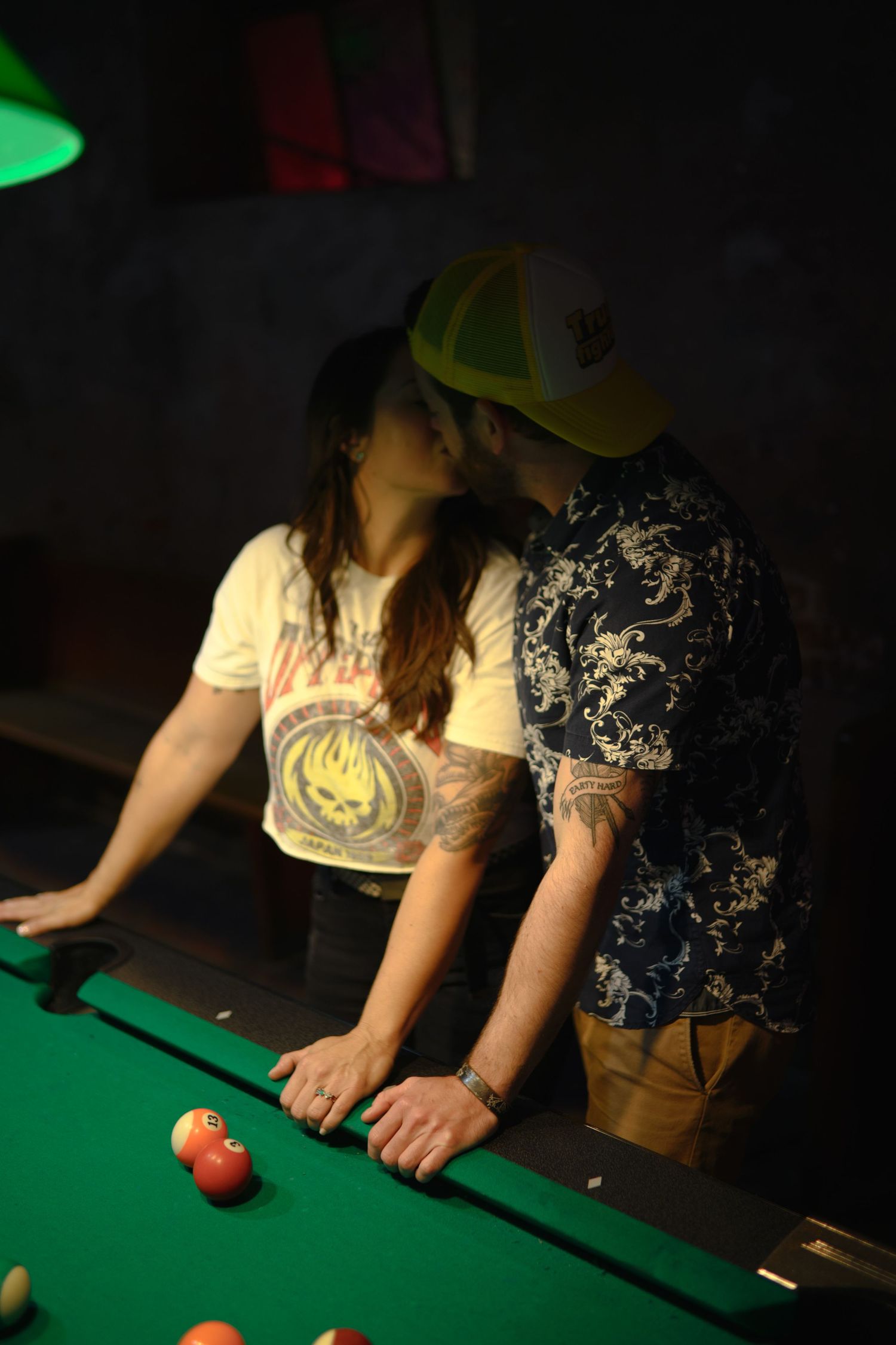 Players leaning over a green felt pool table preparing shots in a dimly lit bar setting.
