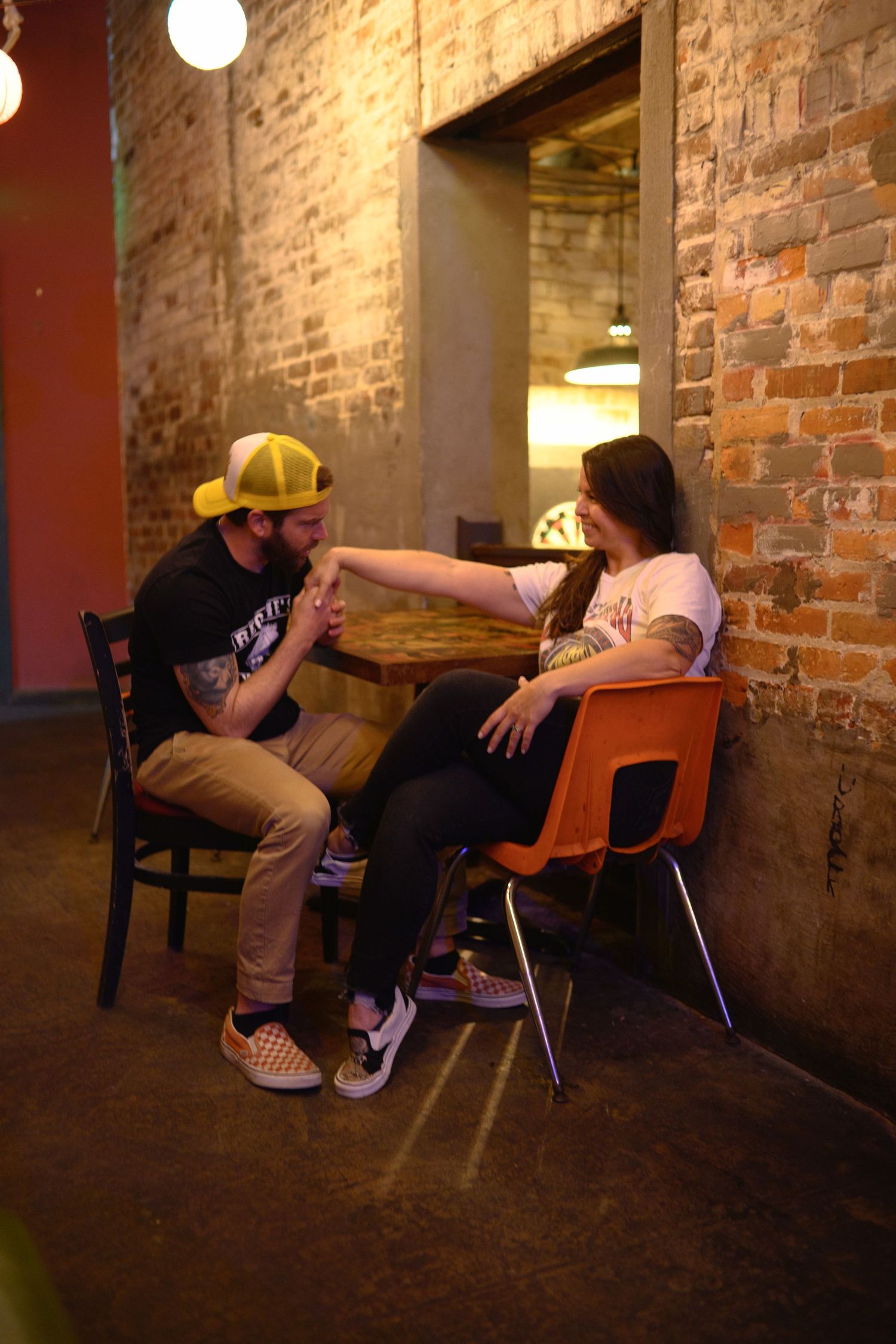 Two people having an animated conversation while sitting in chairs against a rustic brick wall.