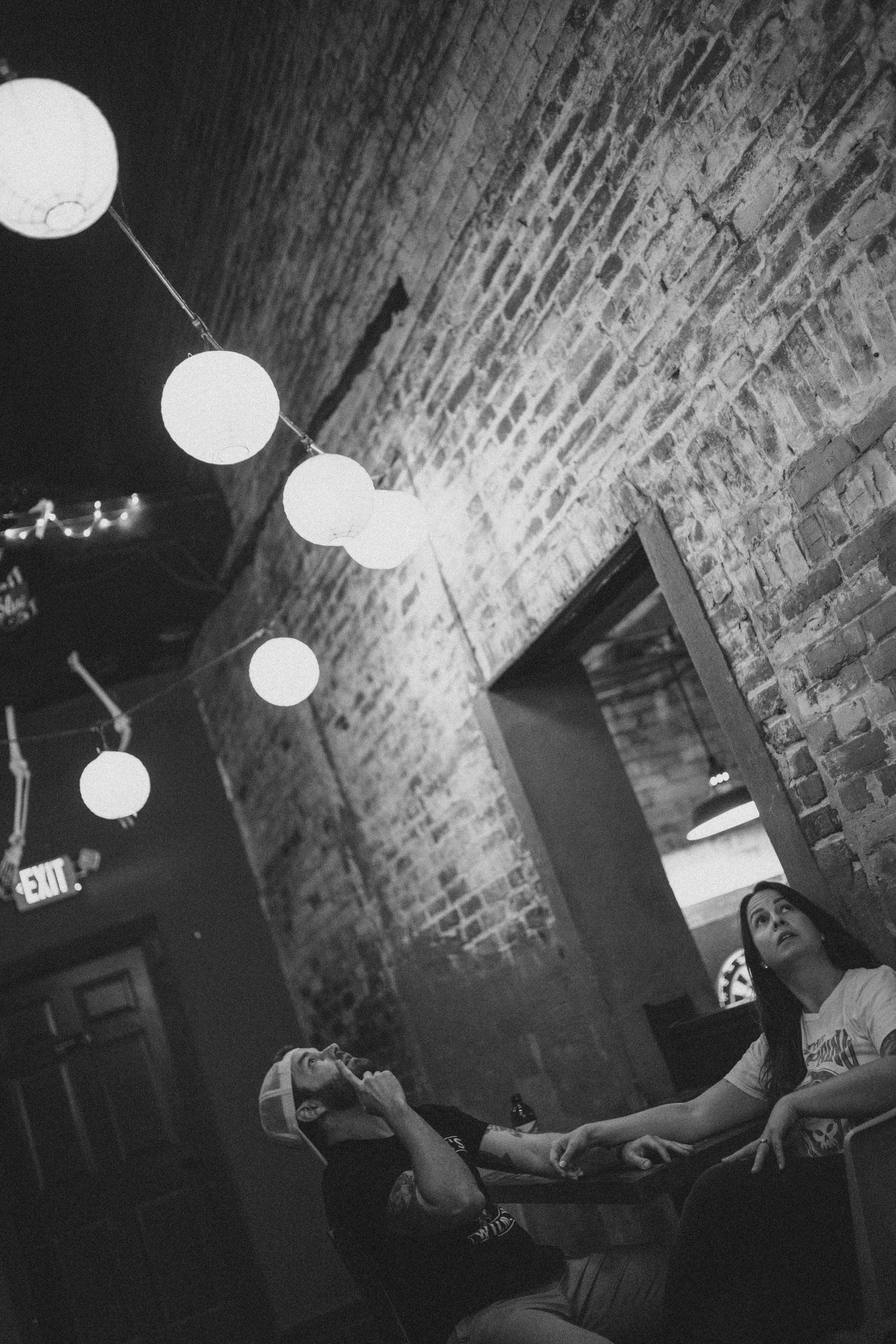 Glowing white paper lanterns hang from a brick ceiling in a dimly lit room.