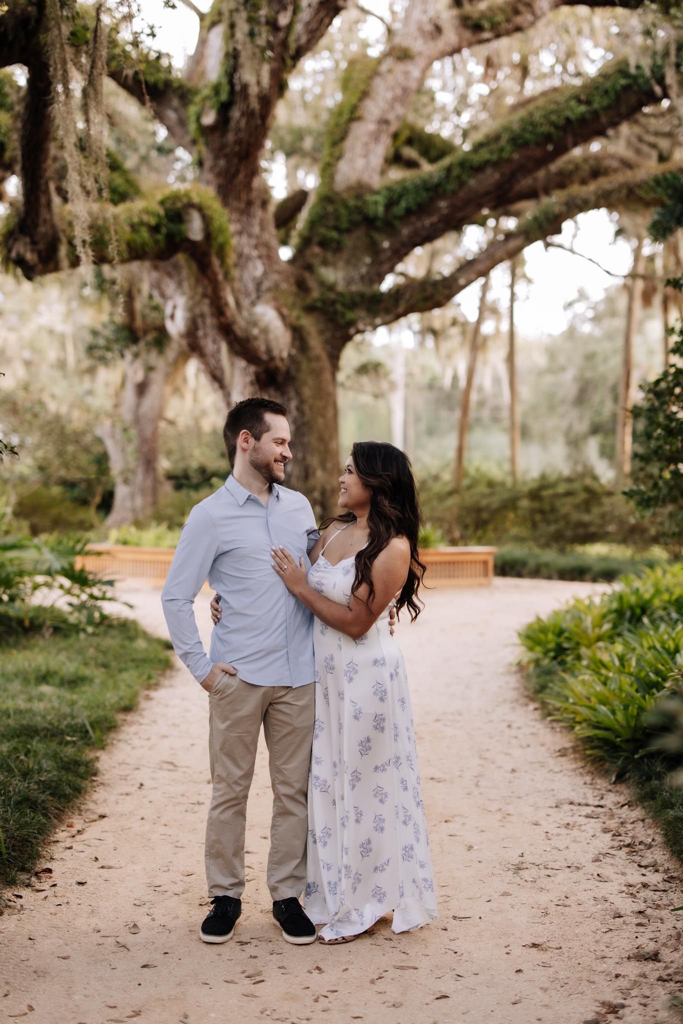 A couple shares romantic moments together while walking along a winding sandy path surrounded by lush trees.
