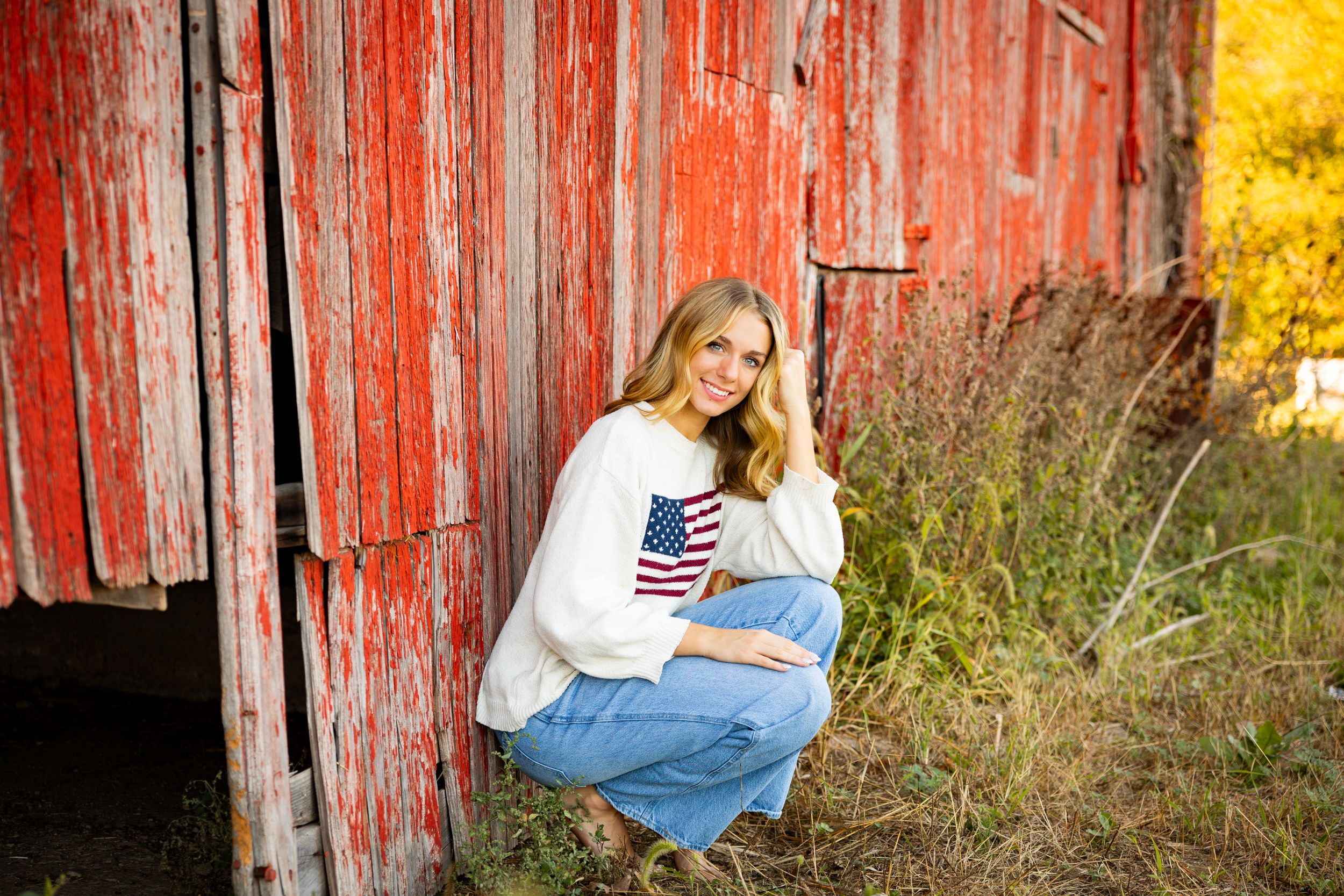 A rustic photoshoot against a weathered red barn wall in autumn with golden foliage in the background.