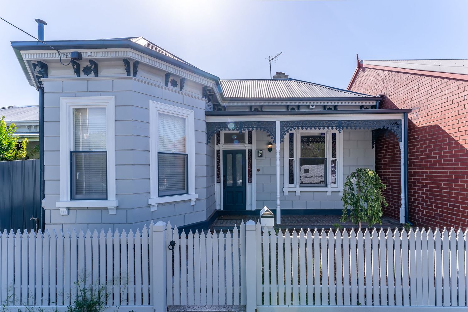 Charming Victorian-style grey weatherboard home with white picket fence and decorative lacework facade.