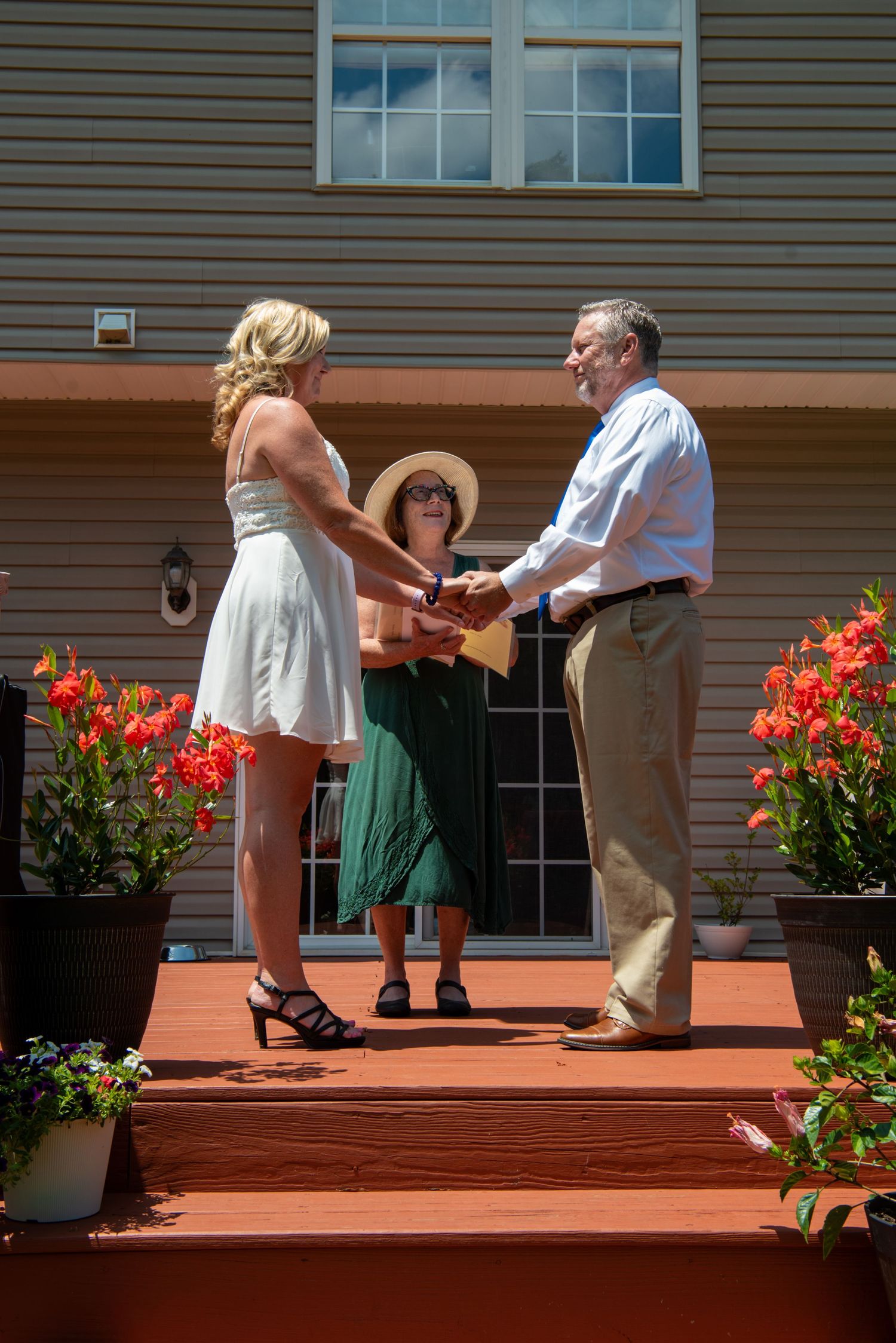 A couple dancing on wooden deck stairs with bright red flowers in planters on a sunny day.