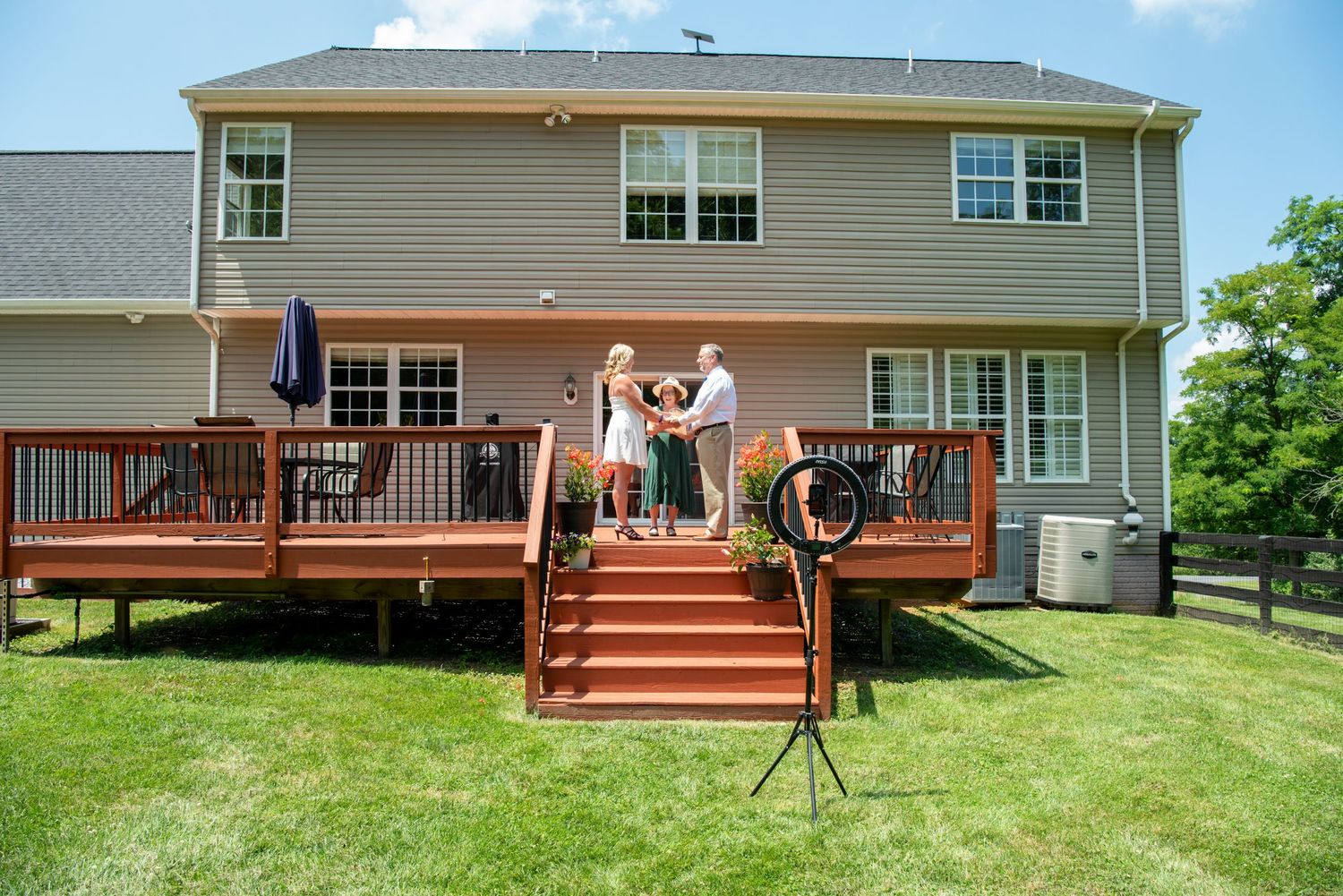 A panoramic view of a residential backyard with a wooden deck, green lawn, and trees in the background.