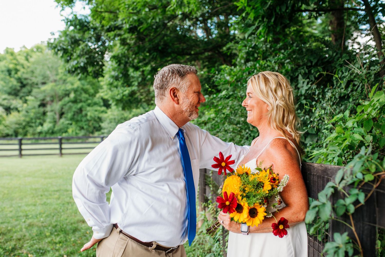 A couple shares romantic moments in a garden setting while holding bright sunflower bouquets and wearing wedding attire.