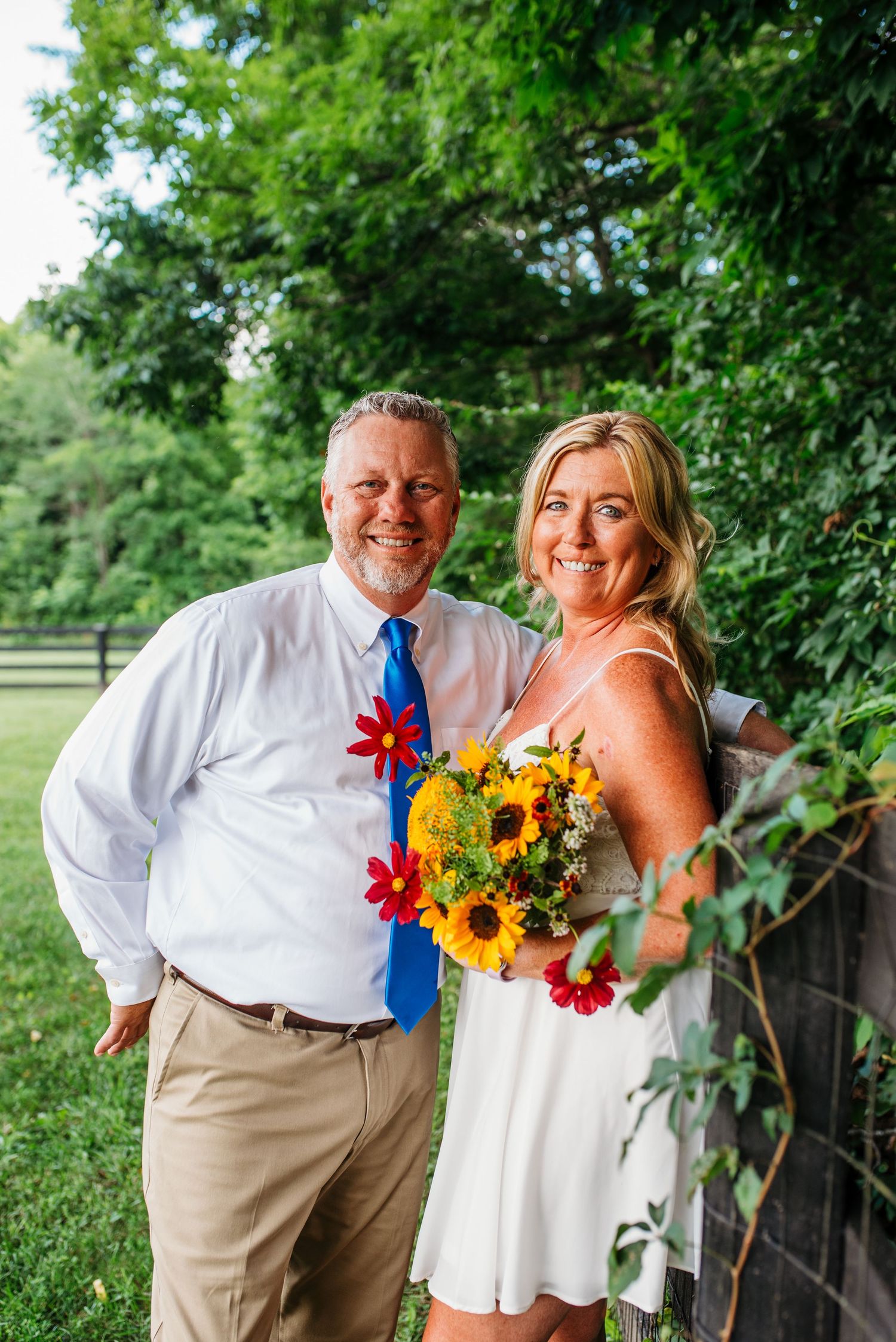 A summer outdoor portrait with sunflowers and bright blue accents against a green backdrop.